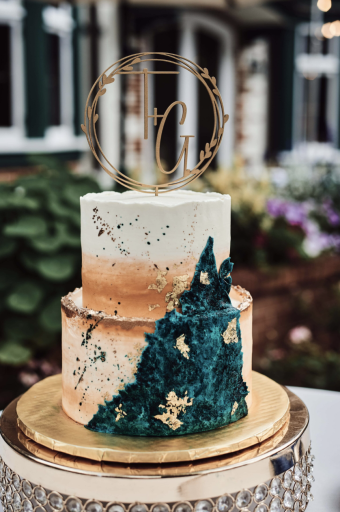 Gold and emerald green decorated two tiered wedding cake sitting on a gold and jeweled cake stand.